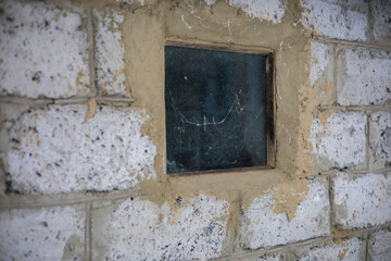 Spider Window in Brick Wall A small, dirty window set into an old, weathered white brick wall reflects the darkness and shows signs of age and neglect, perhaps hinting at abandonment or disrepair.