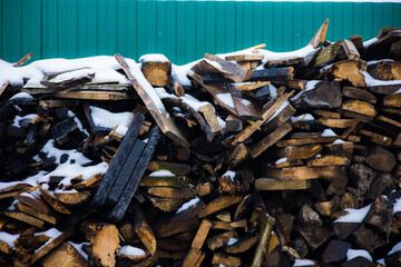 A pile of charred boards after a fire. Snow covering a pile of charred boards near a green fence...