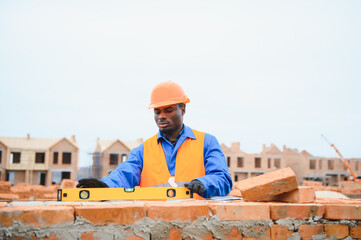 African american construction worker. Portrait of mason bricklayer installing red brick with trowel putty knife outdoors