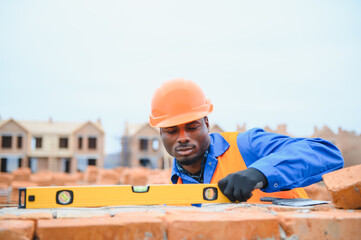 African american construction worker. Portrait of mason bricklayer installing red brick with trowel...