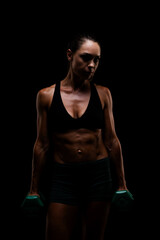 Fototapeta premium Athletic Woman Lifting Dumbbells in a Dark Background Highlighting Strength