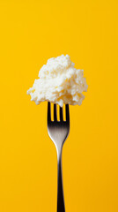 Cottage cheese on a fork tip against yellow background
