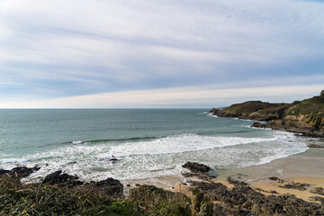 Scène hivernale à la plage du Minou, avec l'écume des vagues frappant le sable clair, tandis que les eaux émeraude de la mer d'Iroise se mêlent à un ciel voilé.