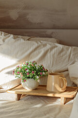 Breakfast in bed: cup of coffee and bouquet on wooden tray. Window light