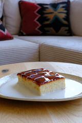 A slice of creamy custard cake topped with caramel and a drizzle of sauce sits on a plate