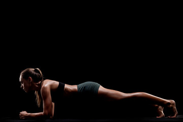 Athletic Woman Performing a Plank Exercise on a Black Background to Display Strength and Fitness