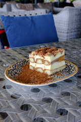 A delightful slice of tiramisu dusted with cocoa powder rests on an ornate plate