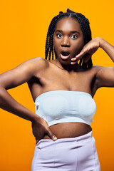 Shocked young woman with braided hair in a strapless top and pastel pants, posing against a vibrant...