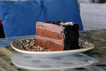 A decadent slice of chocolate layer cake adorned with chocolate shavings sits on a patterned plate