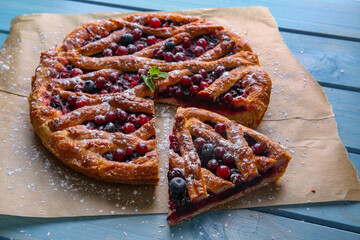 Delicious cut currant pie and fresh berries on blue wooden table