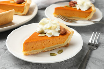 Pieces of tasty homemade pumpkin pie with whipped cream, seeds and nuts on grey table, closeup