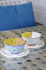 Two bowls of sweet dessert topped with pistachios and nuts sit on a glass table