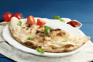 Tasty calzone with basil, tomatoes and sauce on blue wooden table, closeup