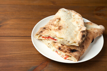 Halves of tasty calzone with meat, cheese and tomato on wooden table, closeup. Space for text