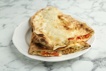 Halves of tasty calzone with meat, cheese and tomato on white marble table, closeup