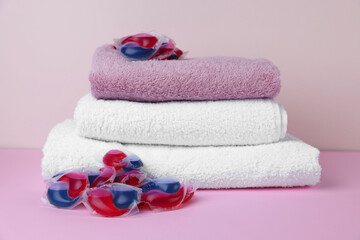 Laundry detergent capsules and clean towel on pink background