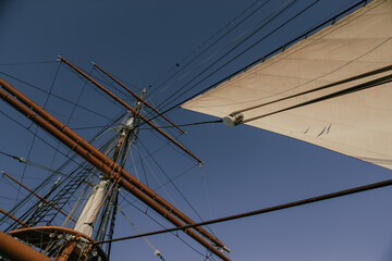 Fototapeta premium Tall Ship Sails and Rigging along the Harbor under a Cloudless Blue Sky