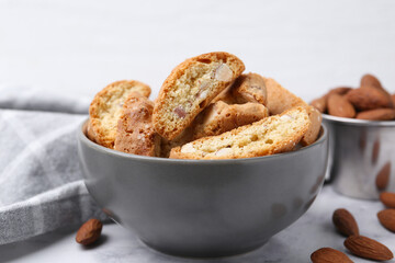 Tasty almond biscuits (Cantuccini) in bowl and nuts on light table, closeup