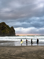Group of young women with surfboards, gazing at the waves in New Zealand. A moment of anticipation, adventure, and connection to the ocean.