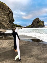 Man with surfboards, gazing at the waves in New Zealand. A moment of anticipation, adventure, and connection to the ocean.