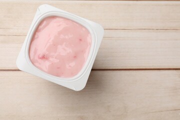 Delicious yogurt in plastic cup on wooden table, top view. Space for text