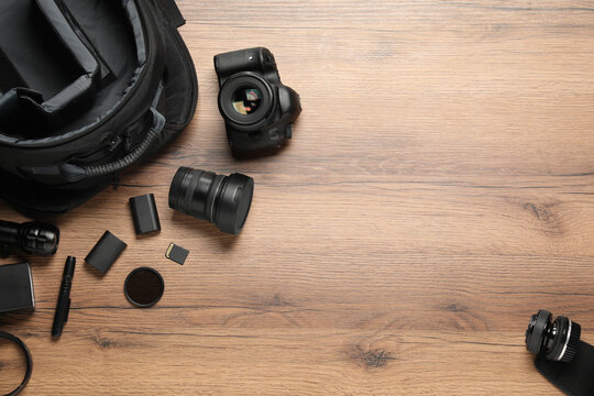 Professional photographer's equipment and backpack on wooden background, flat lay. Space for text