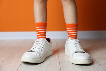 Child wearing oversized sneakers near orange wall indoors, closeup