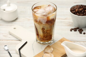 Refreshing iced coffee with milk in glass and beans on white wooden table, closeup
