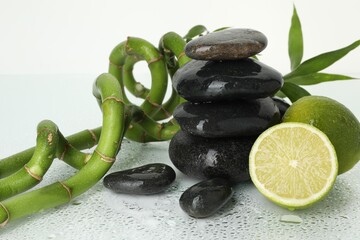 Spa composition with limes, massage stones and bamboo stems on wet surface against white background, closeup