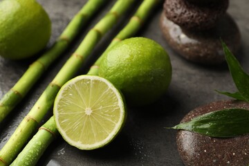 Spa composition with wet limes, pebble stones, bamboo leaves and stems on grey table, closeup