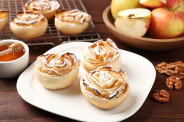 Tasty apple roses with powdered sugar served on wooden table, closeup