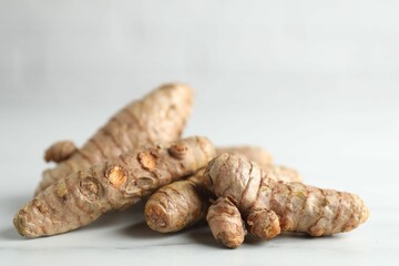 Raw turmeric roots on white marble table, closeup
