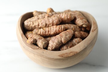 Raw turmeric roots in bowl on white marble table, closeup