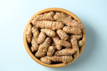 Tumeric rhizomes in bowl on light blue background, top view