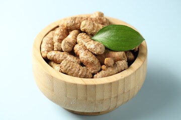 Tumeric rhizomes with leaf in bowl on light blue background, closeup