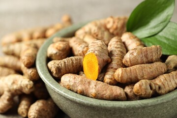 Tumeric rhizomes with leaves in bowl on grey table, closeup