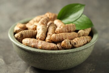 Tumeric rhizomes with leaves in bowl on grey table, closeup