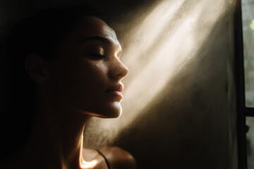 Dramatic portrait of a woman illuminated by a ray of light in a dark setting, evoking themes of hope, introspection, spirituality, and emotional depth