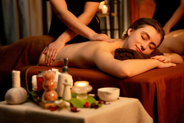 Caucasian couple customer enjoying relaxing anti-stress spa massage and pampering with beauty skin recreation leisure in warm candle lighting ambient salon spa at luxury resort or hotel. Quiescent