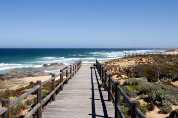 A serene and picturesque wooden road leading through lush greenery toward a beautiful beach along the Rota Vicentina in Portugal.