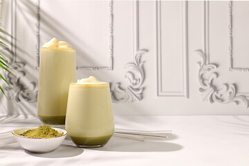 Green tea matcha latte with milk on elegant kitchen sunny background with palm leaves and matcha powder. Traditional Indian drink rich in antioxidants used for weight loss and treatment,
