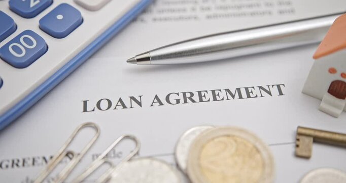 Loans, financial agreements, and real estate transactions. A close-up of a loan agreement document with a calculator, coins, a house model, and a key, representing financial planning, real estate, etc