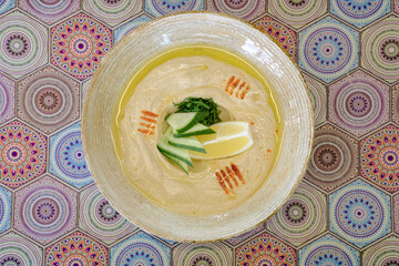Creamy hummus garnished with cucumber lemon and a sprinkle of spice served in a bowl