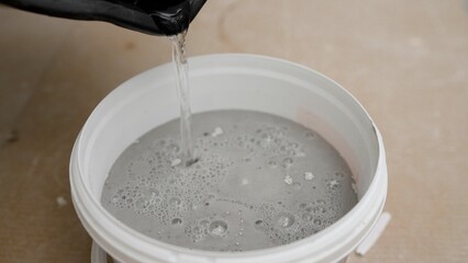 Construction worker pouring water into bucket with gray cement mixture