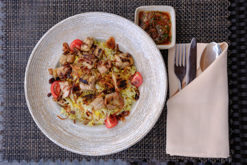 Grilled chicken and rice dish garnished with fried onions and cherry tomatoes Served with a small bowl of red sauce