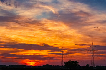 Summer sunset with a dramatic sky and overland high voltage lines near Tabertshausen, Aholming, Deggendorf, Bavaria, Germany