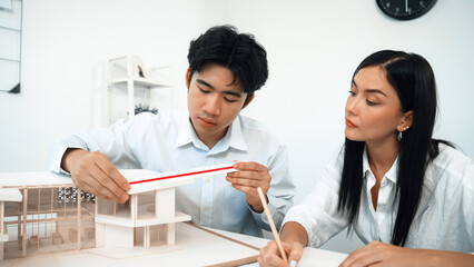 Professional male engineer measure house model by using ruler while beautiful cooperative coworker...
