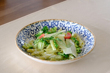Creamy pasta dish with broccoli and cherry tomatoes garnished with shaved cheese