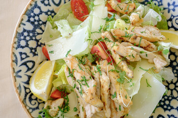 Grilled chicken and romaine lettuce salad with shaved parmesan cheese cherry tomatoes and lemon wedges