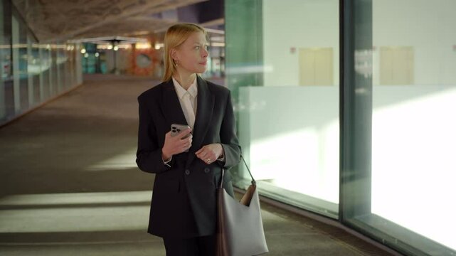 Skilled professional woman in an elegant business suit stands confidently in a modern office, checking her smartphone as she prepares for a productive workday full of opportunities and challenges